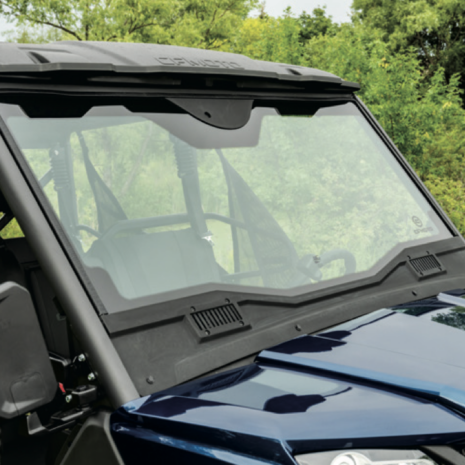 A clear glass windshield installed on a blue utility vehicle, with trees in the background.