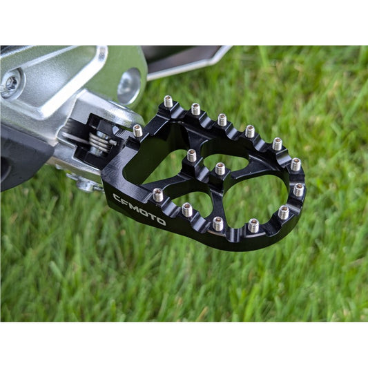 Black motorcycle foot peg with 'CFMOTO' branding on a grass background